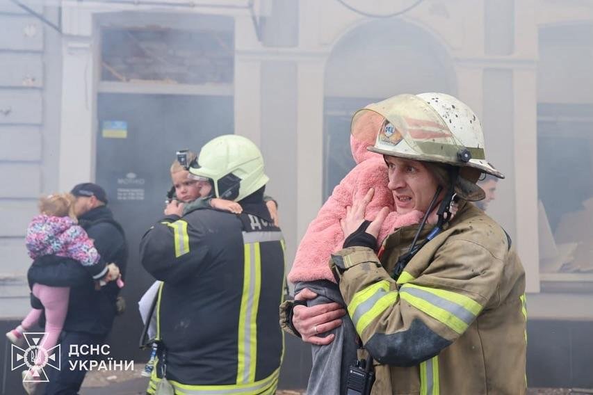 Rescuer carrying girl near fire truck after drone strike in Kharkiv